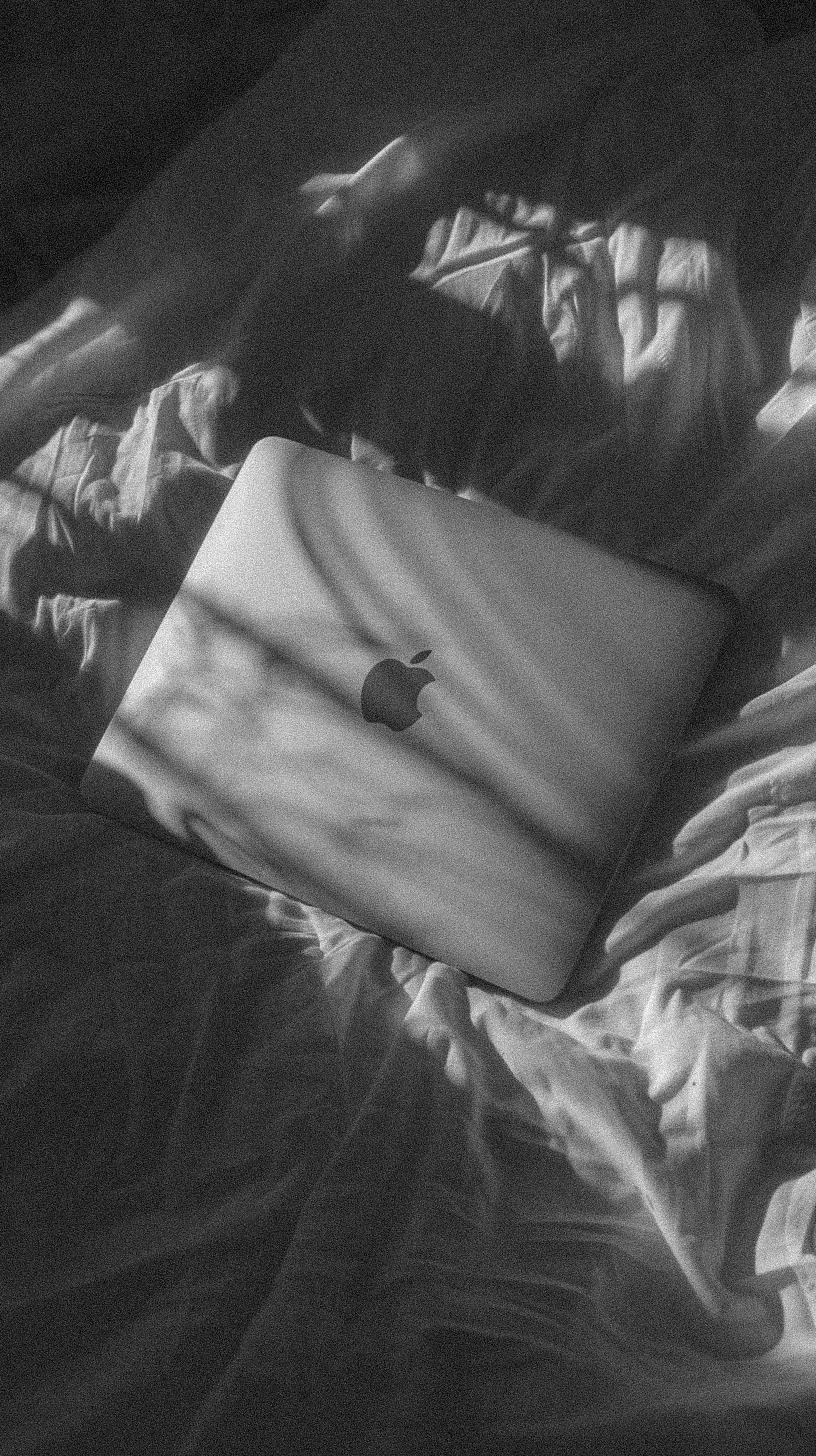 Apple Laptop auf zerknüllter weißer Bettwäsche, Schwarz-Weiß